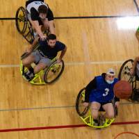 Adults in wheelchairs watching basketball in the air.